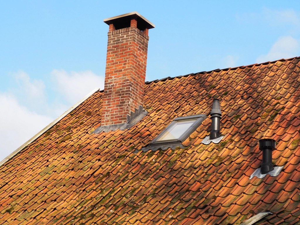 Clay tiled pitched roof with a brick chimney, roof window and vents